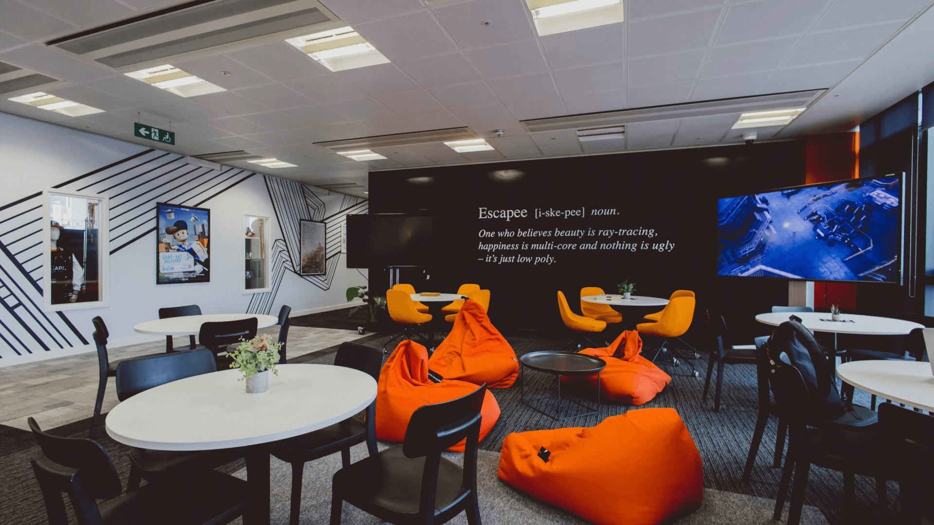 Breakout space with tables, chairs, beanbags, TV screens and a quote printed on the wall