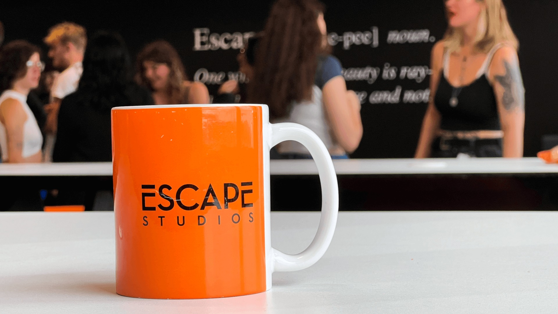 Escape Studios orange mug on a table with students talking in the background