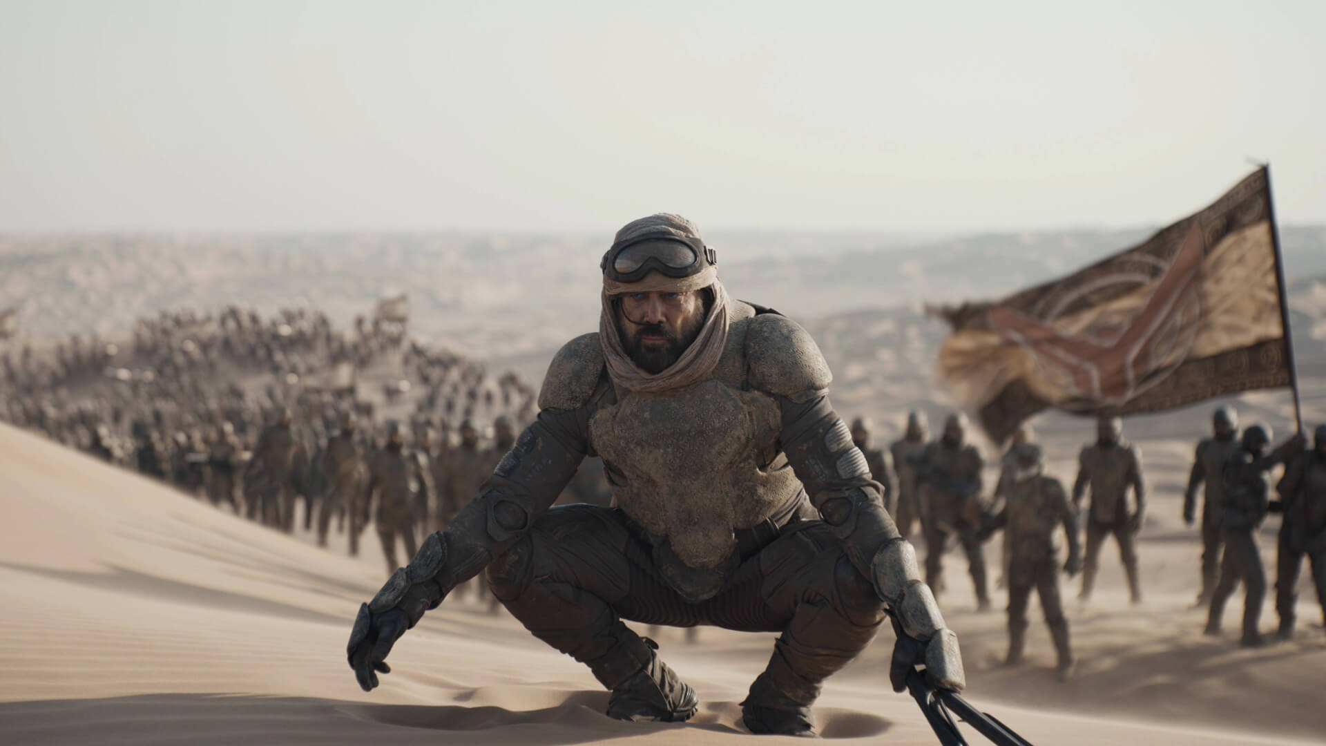 A man in armour squatting in fron of an army in the desert